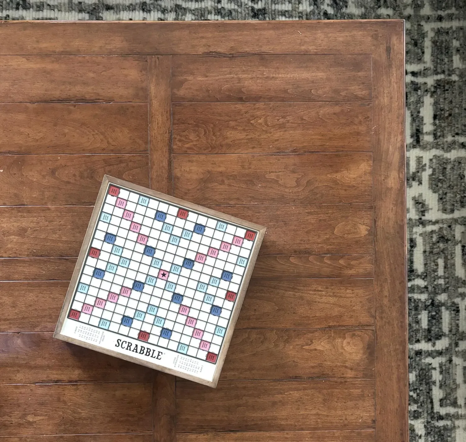 A Scrabble board on a wooden table next to a patterned rug