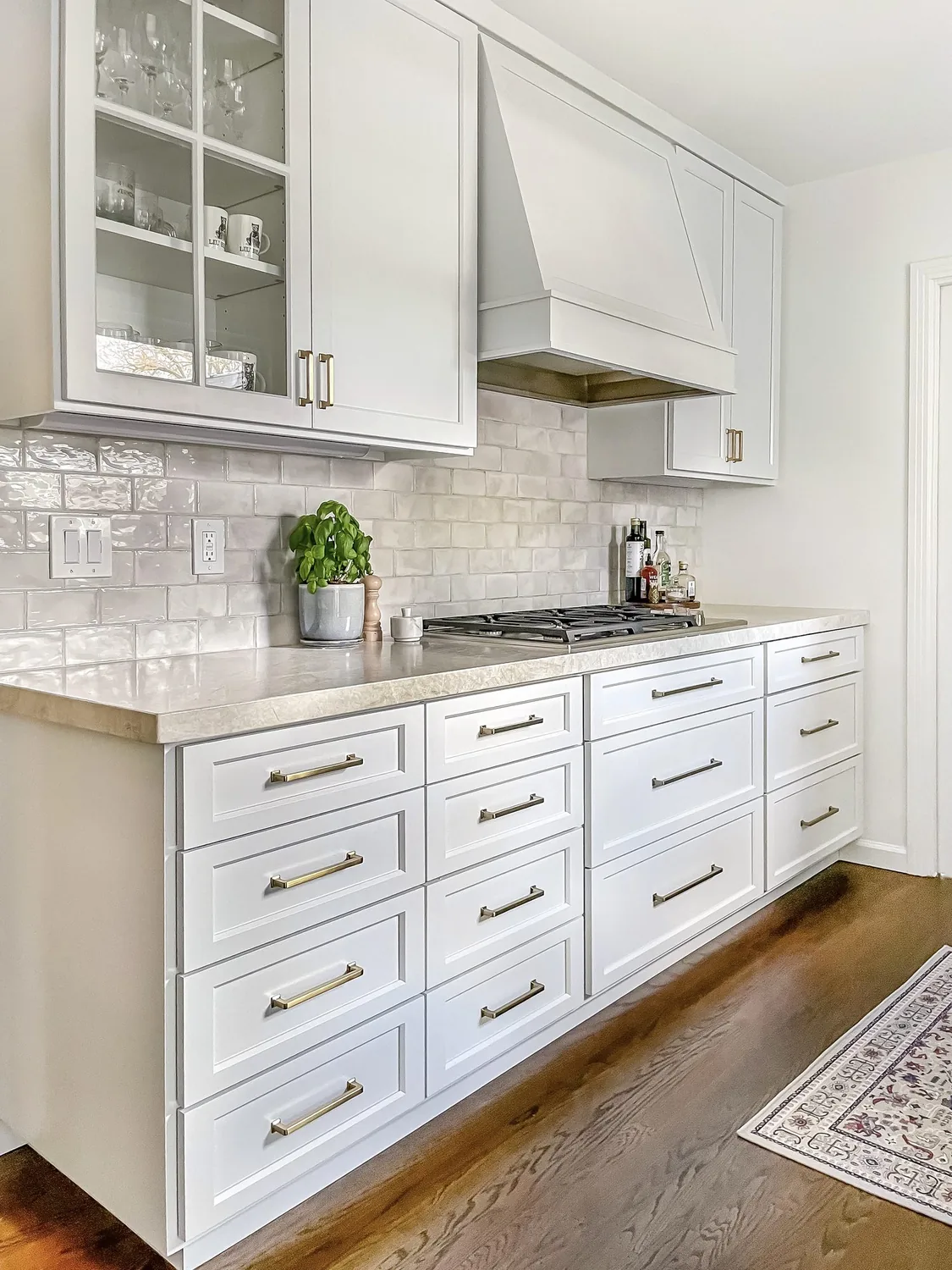 A modern kitchen corner with white cabinets, marble countertops, a wine bottle and glass, cutting boards, a plant