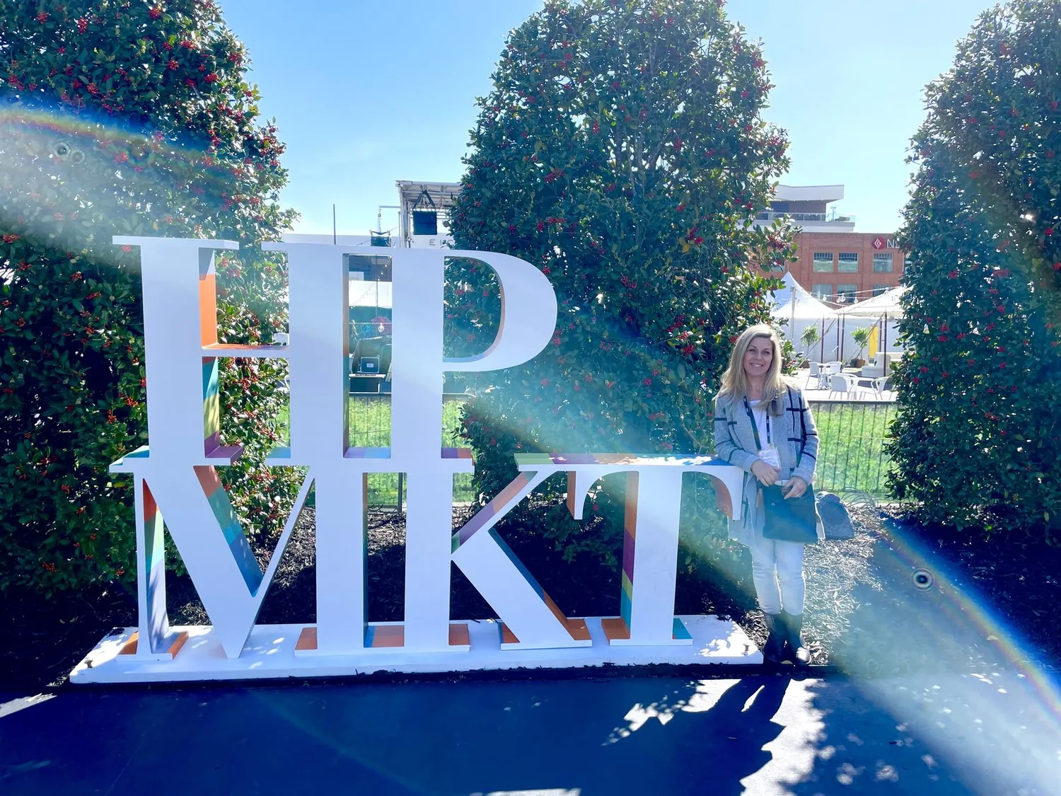 A woman stands next to large white letters spelling 'HP VIKI' outdoors with greenery and event tents in the background