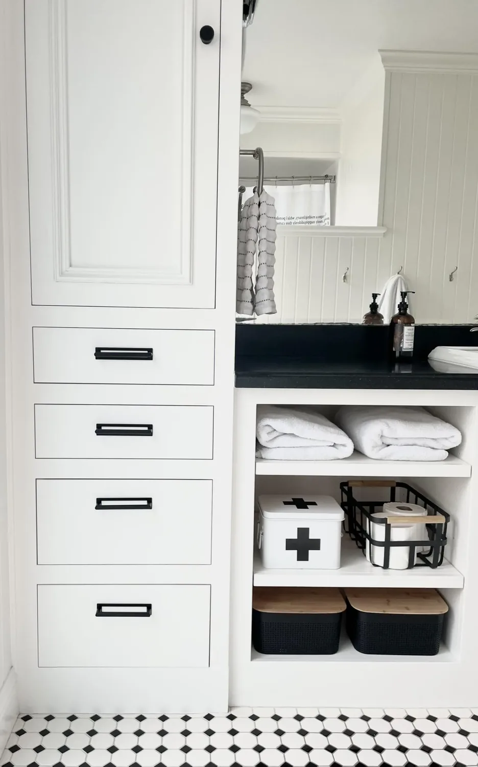 A clean, organized bathroom vanity area with white cabinetry, black countertop, folded towels, and storage baskets