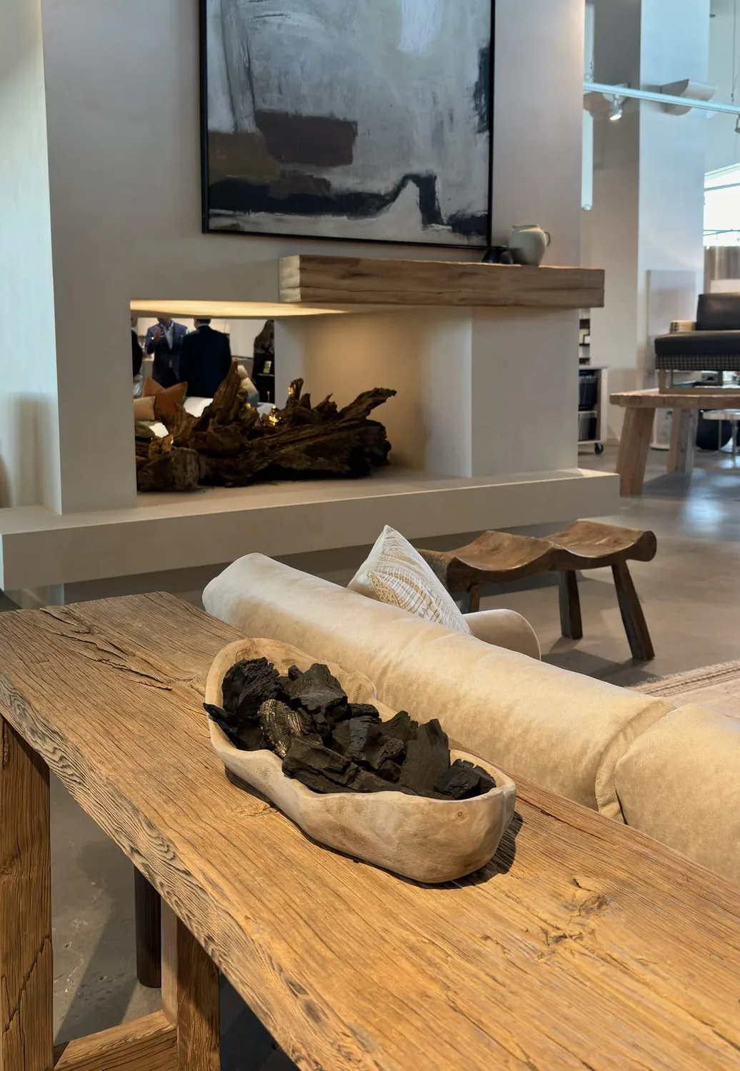 A modern living room featuring a rustic wooden table with a decorative bowl, a beige sofa, a contemporary fireplace with driftwood, and abstract wall art