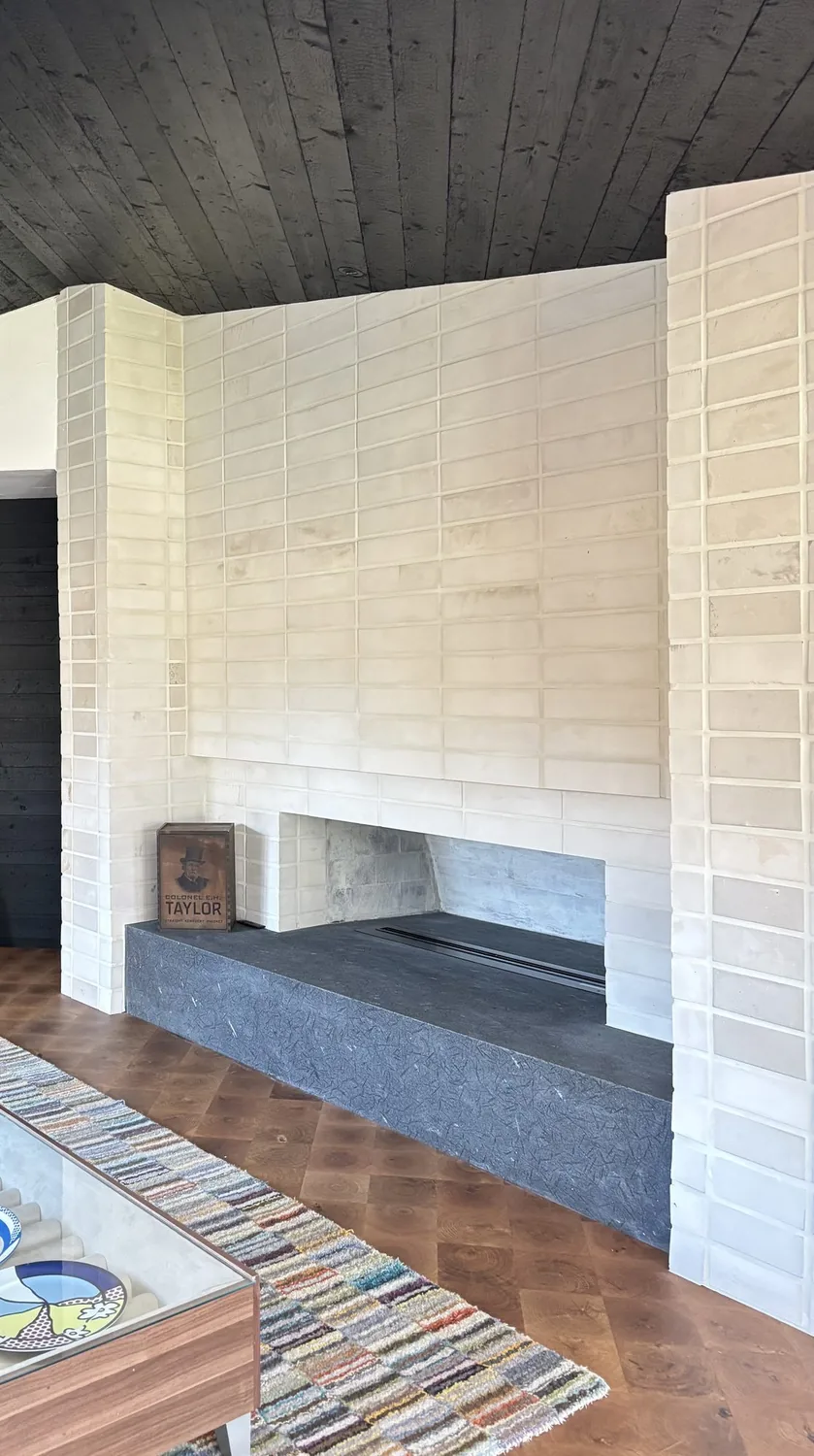 A modern living room featuring a white tiled fireplace with a dark stone hearth, a colorful striped rug, and a wooden
