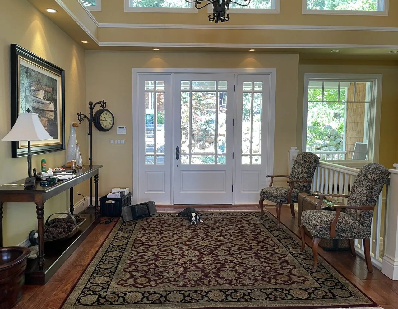 A traditional entryway with a large patterned rug, two upholstered chairs, a wooden console table with a lamp