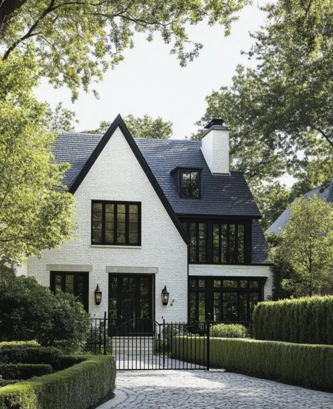 A modern white brick house with black framed windows and a black roof, surrounded by manicured hedges and trees