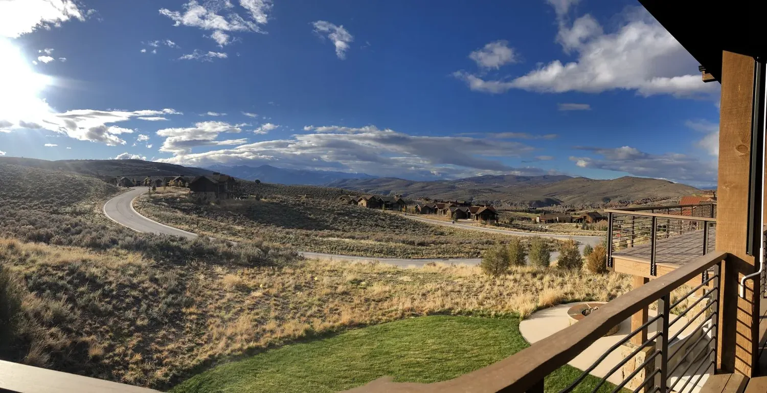 View from a balcony overlooking a winding road, dry grassy hills, scattered houses, and distant mountains under