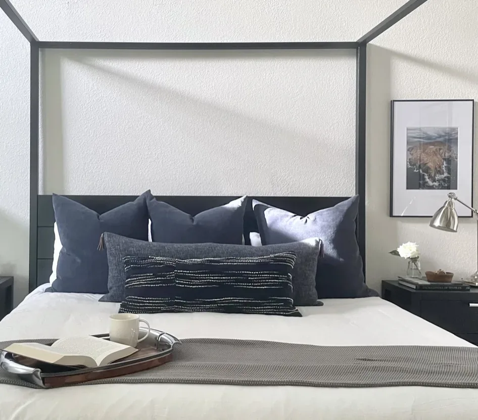 A modern living room corner featuring a white tiled fireplace with a woven basket, a small side table with books