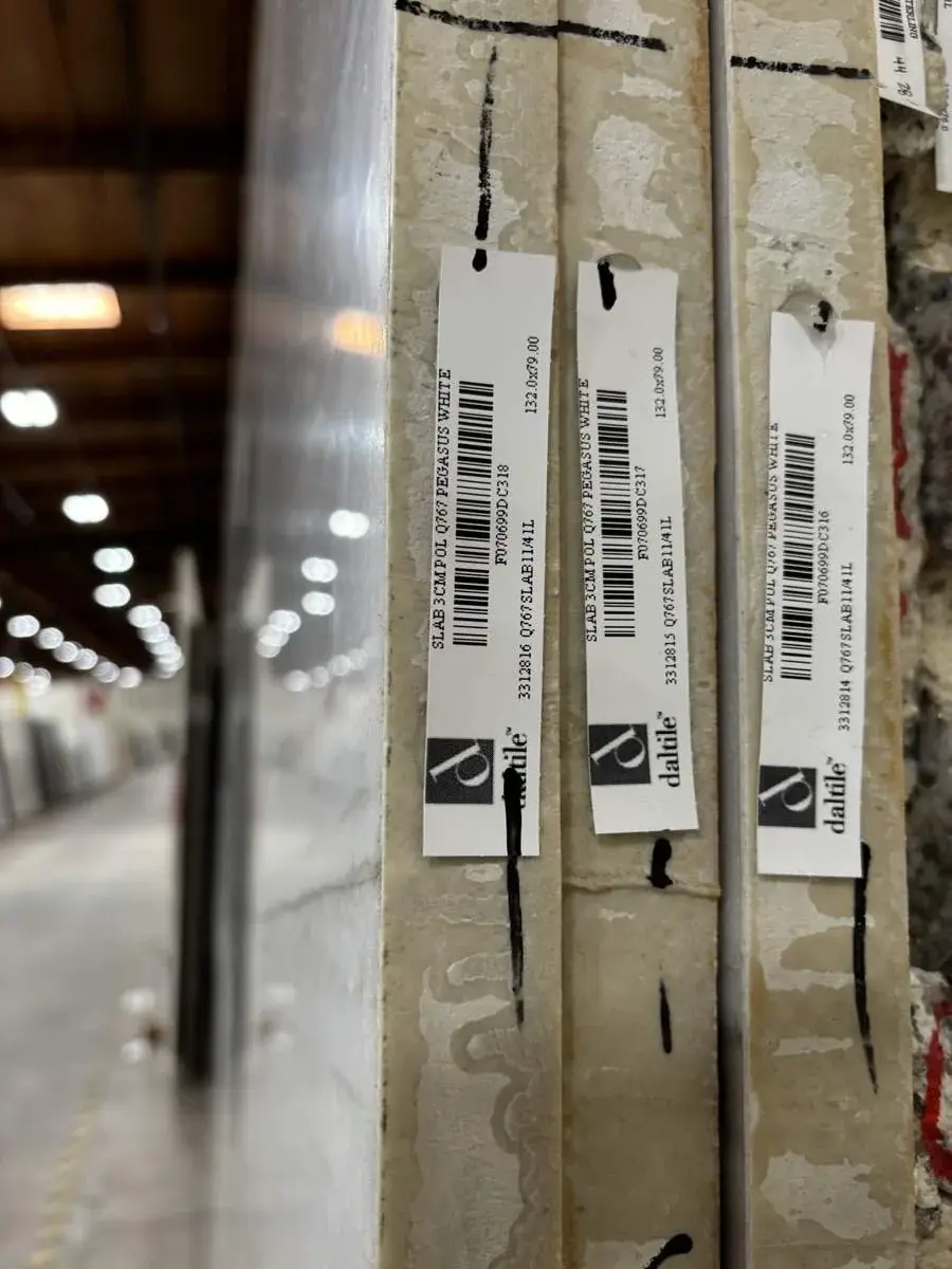Close-up image of stacked slabs of Pegasus White polished stone with Dal Tile labels in a warehouse