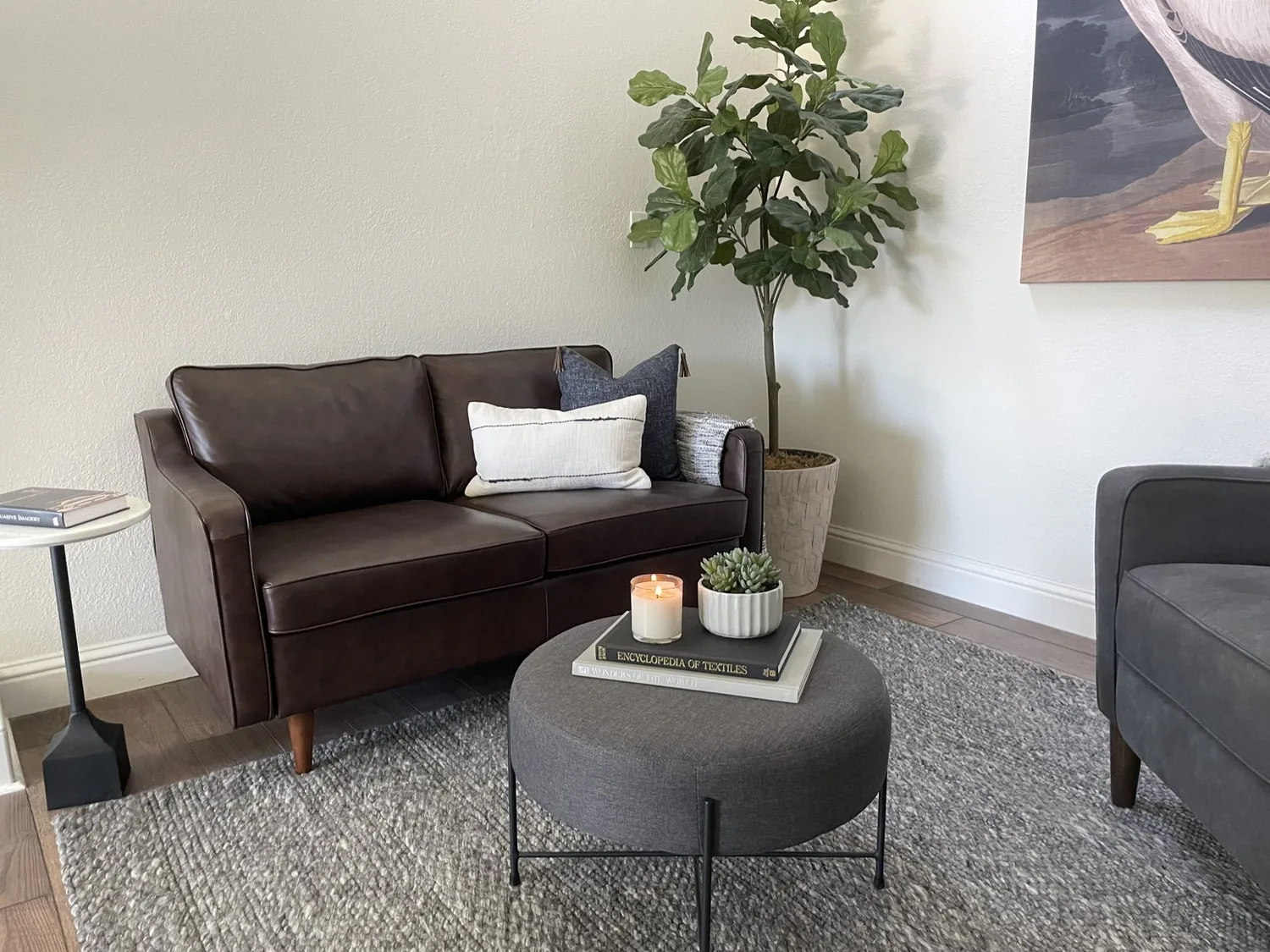 A woman sitting in a cozy living room holding a cup, with a wooden table beside her featuring essential oils