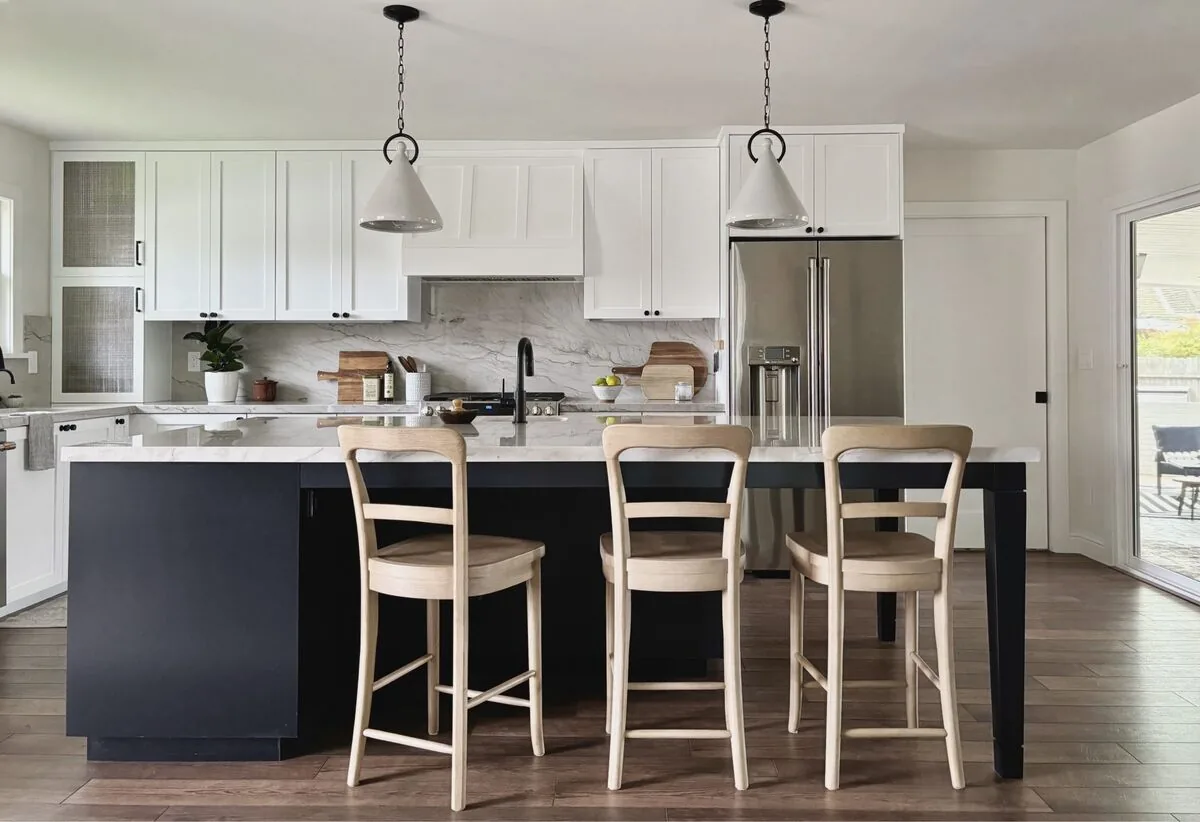 A bright modern kitchen with white cabinetry, brass handles, a black faucet, and a patterned staircase in the background
