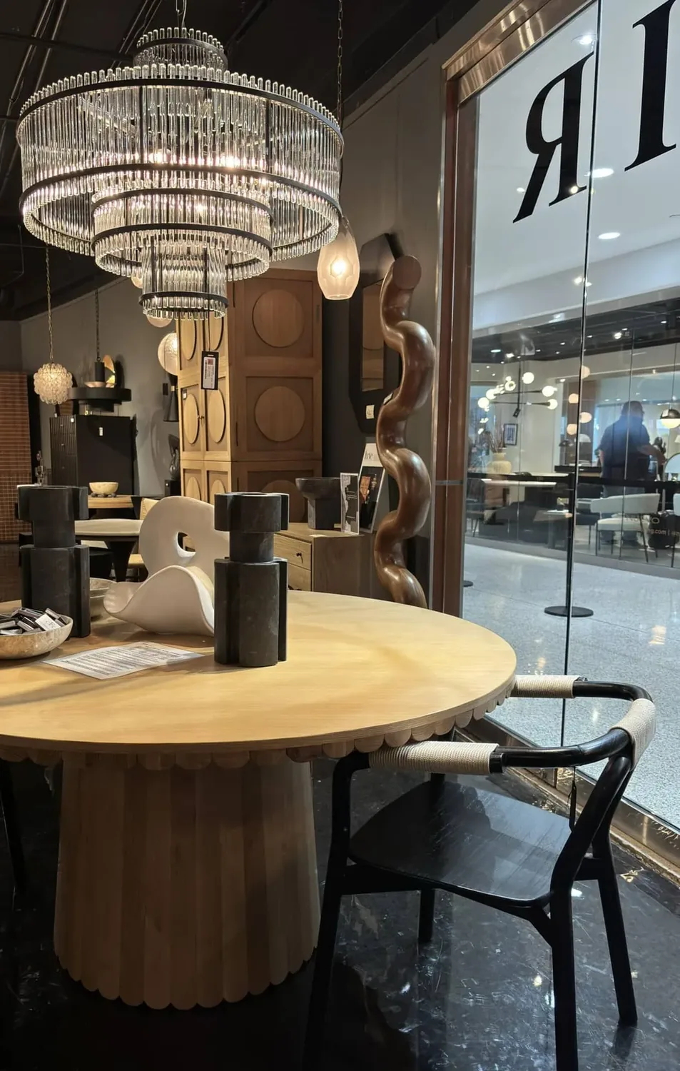 A modern dining room setup featuring a round wooden table, black chairs with woven armrests, a large crystal