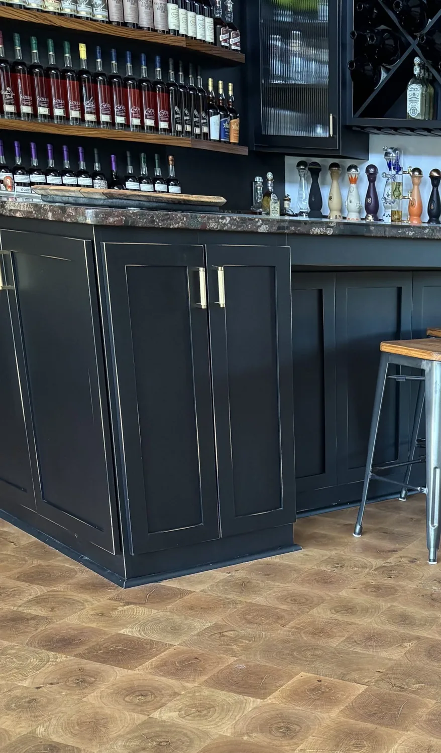 A dark navy shaker-style wet bar with brass hardware, open bottle shelving, and an end-grain wood block floor
