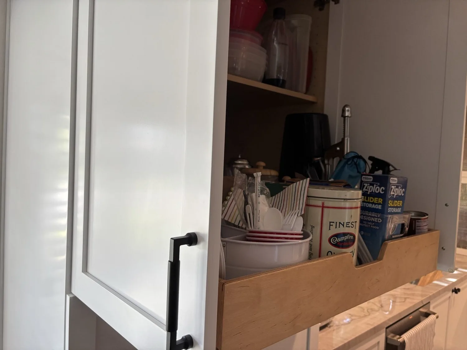 A partially open kitchen cabinet drawer showing organized storage containers, utensils, and food storage items