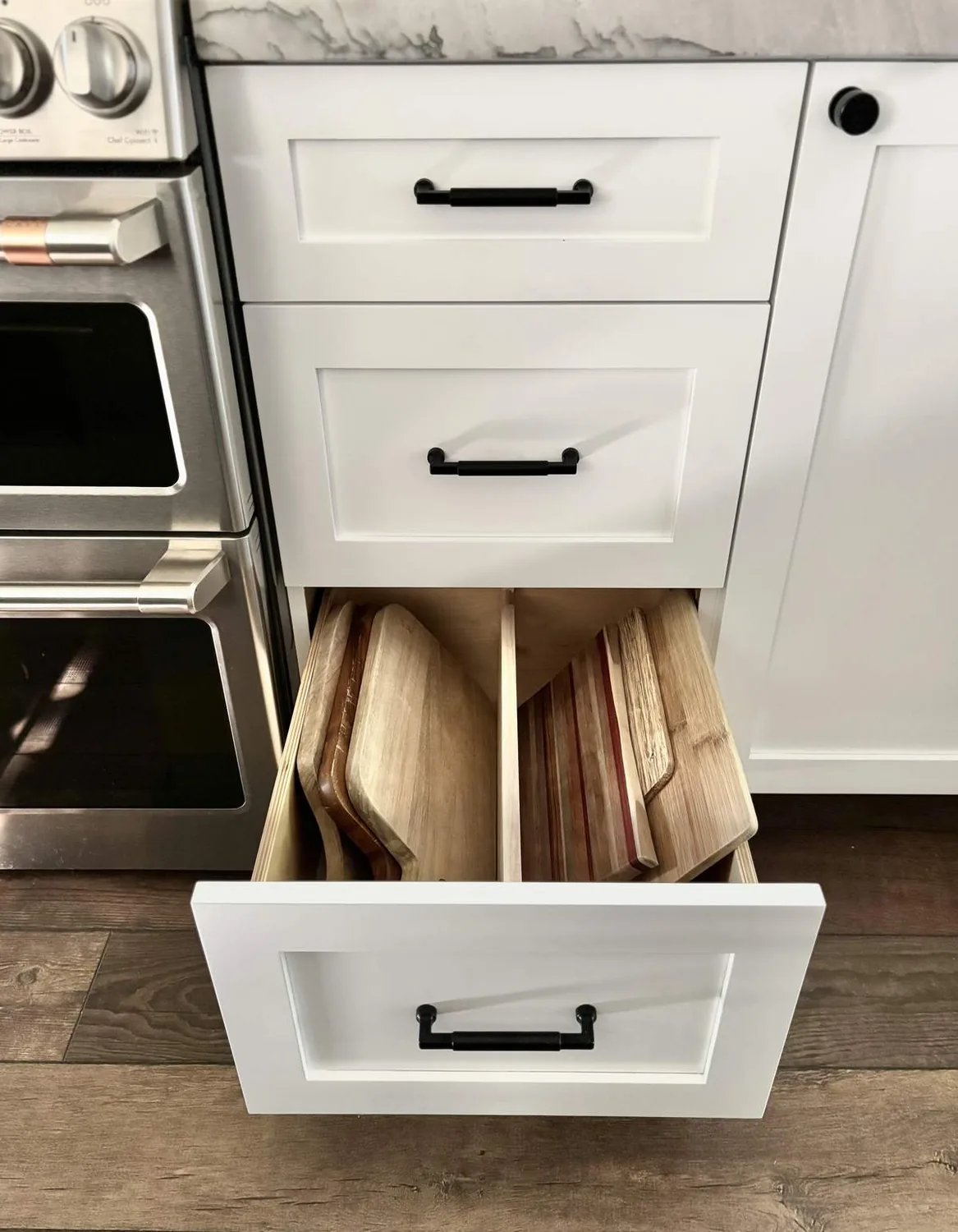 A kitchen drawer open to reveal organized wooden cutting boards next to a stainless steel oven