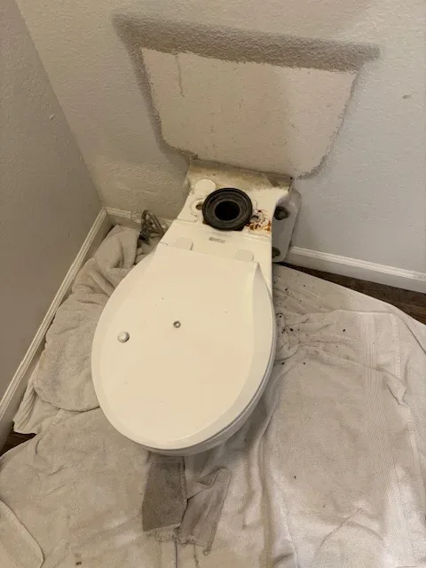 A toilet without a tank installed, placed on a towel-covered floor in a small bathroom corner