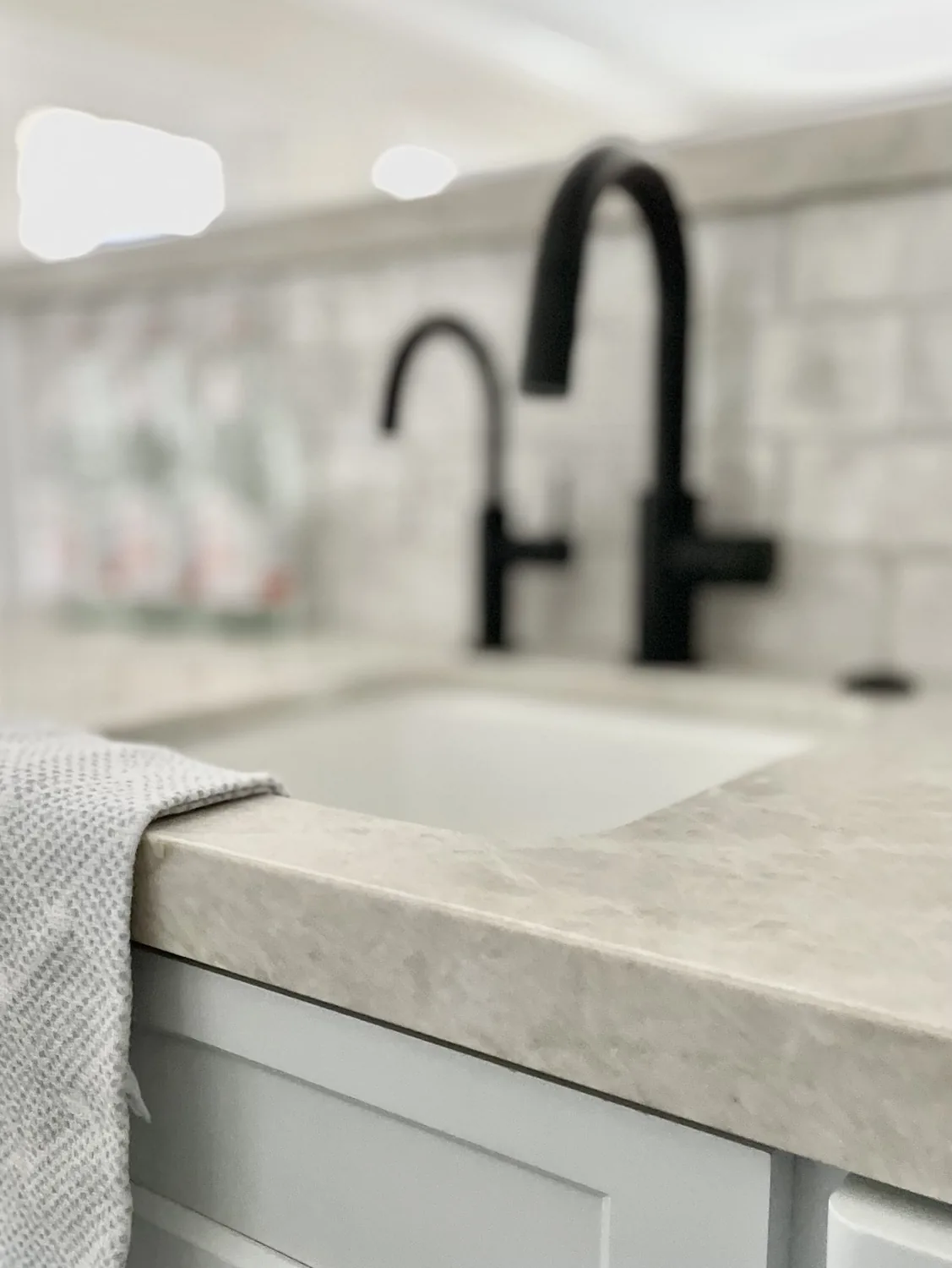 Close-up of a kitchen sink with a beige countertop, black faucets, and a textured towel hanging over the edge