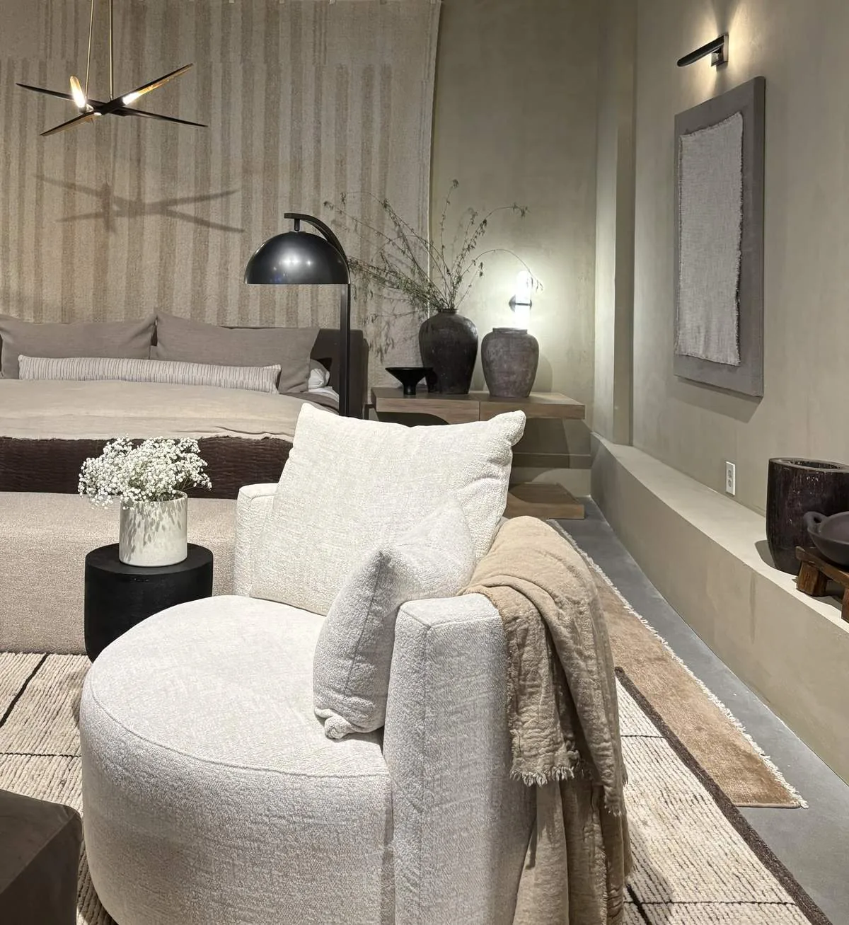 A modern living room with neutral tones featuring a round white armchair, a beige sofa, decorative vases, and minimalist lighting