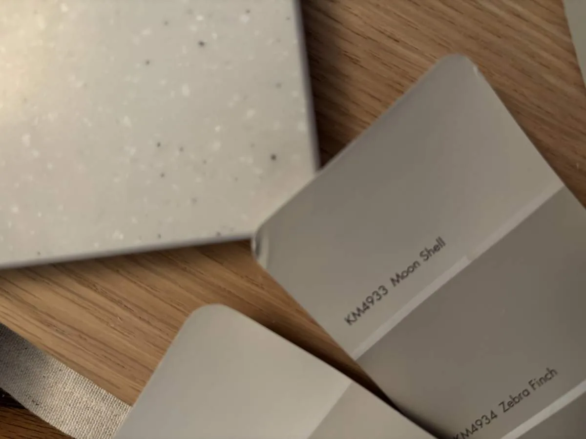 Paint swatches in warm greige tones fanned over a speckled quartz sample on oak flooring