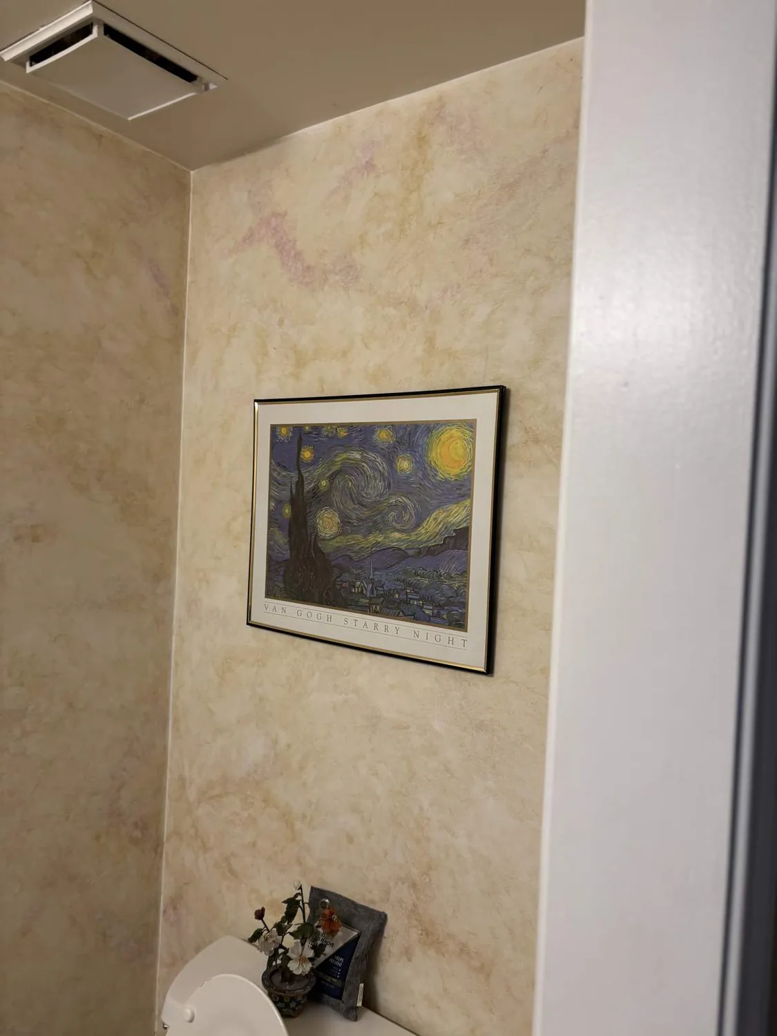 Beige walls, corner toilet. Above hangs a Van Gogh print