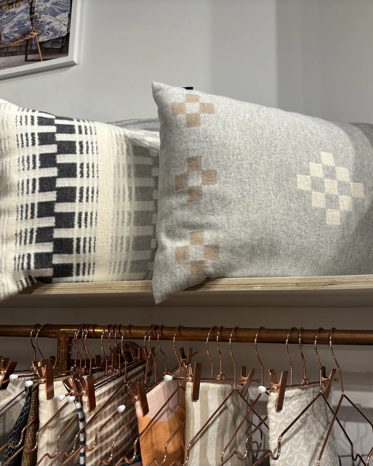 A display of patterned pillows and fabric samples hanging on copper hangers in a retail or showroom setting