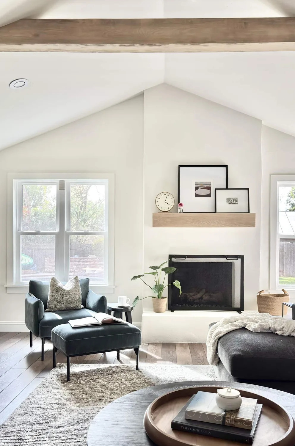 A bright living room with vaulted ceiling, a fireplace, modern furniture, and decorative items on a floating shelf