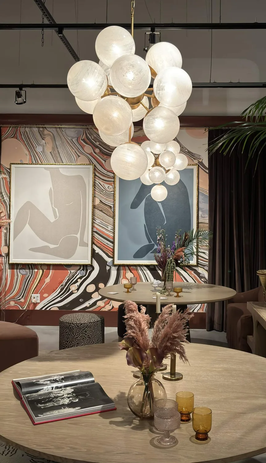 A contemporary dining room with a round wooden table, modern globe chandelier, abstract art, and decorative plants