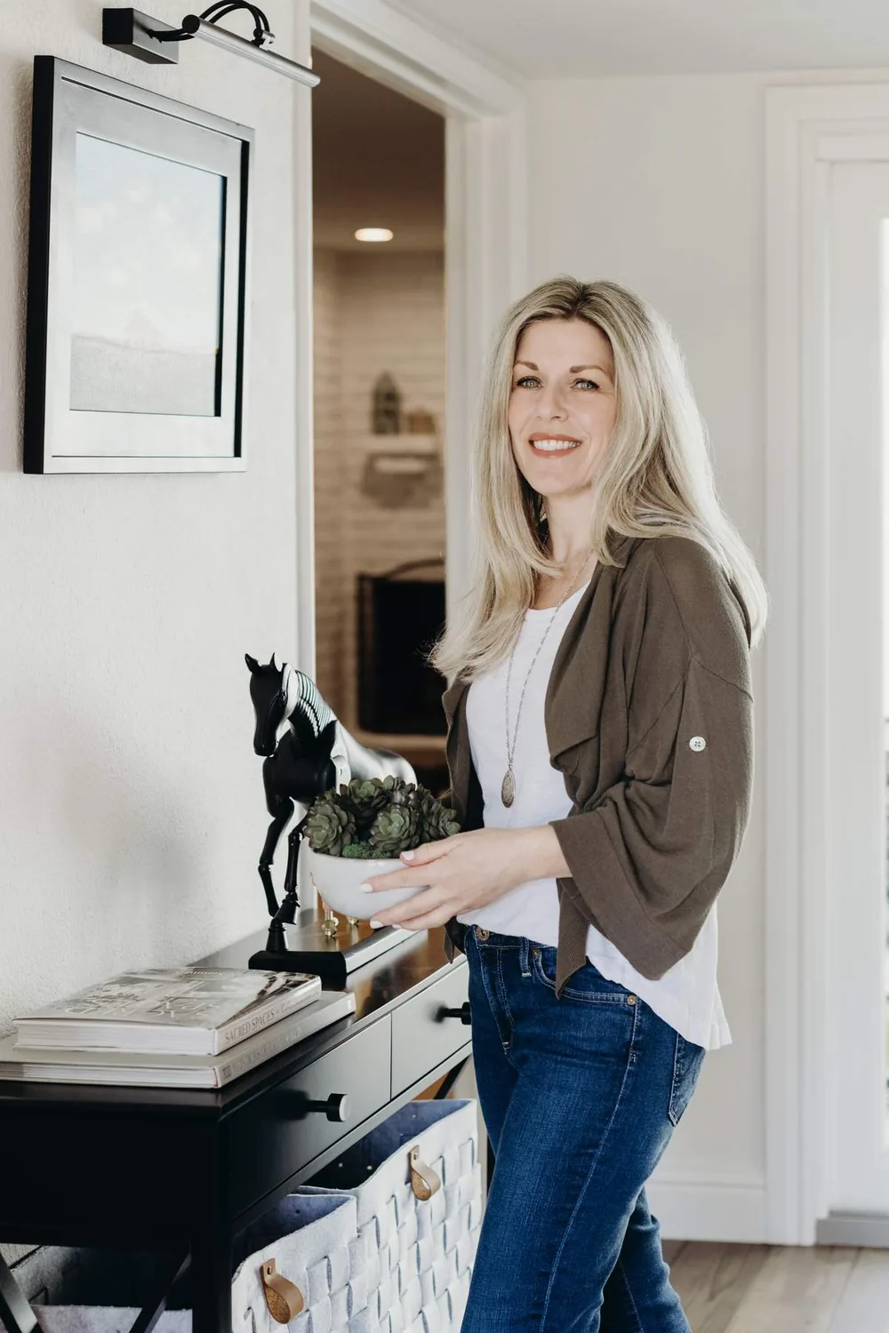 A woman standing next to a black console table with decorative items in a modern living space