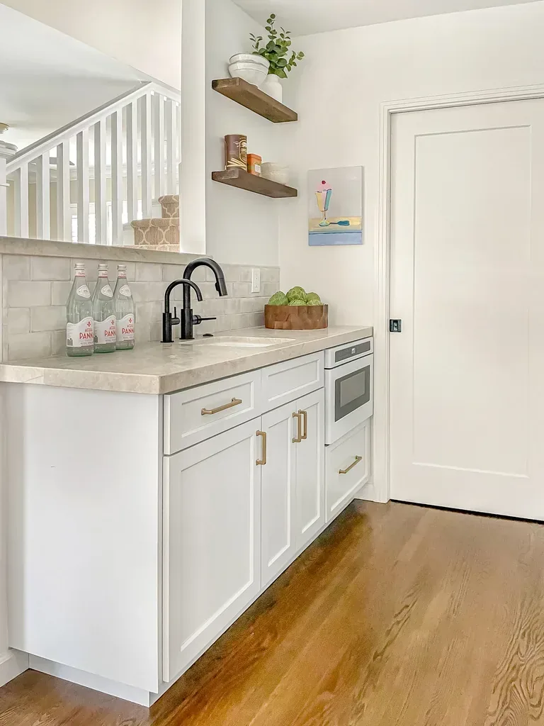 White cabinets with light wood shelves and a small painting stand out in the kitchen corner. Black faucet? Of course