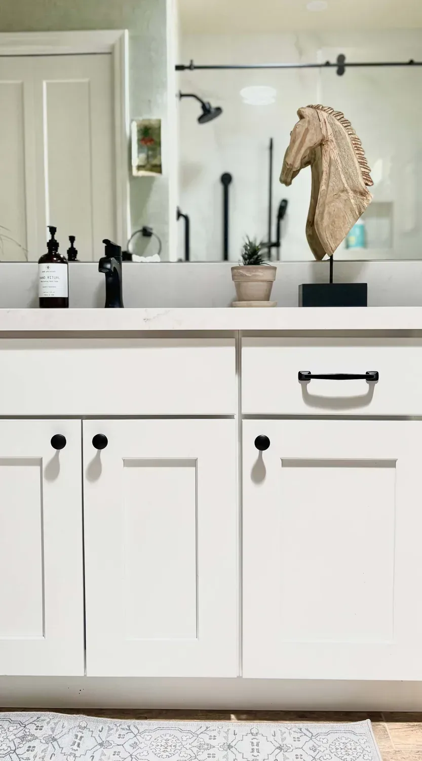 Vanity gets white cabinets with black hardware and faucets. Wooden horse head. Small plant by mirror