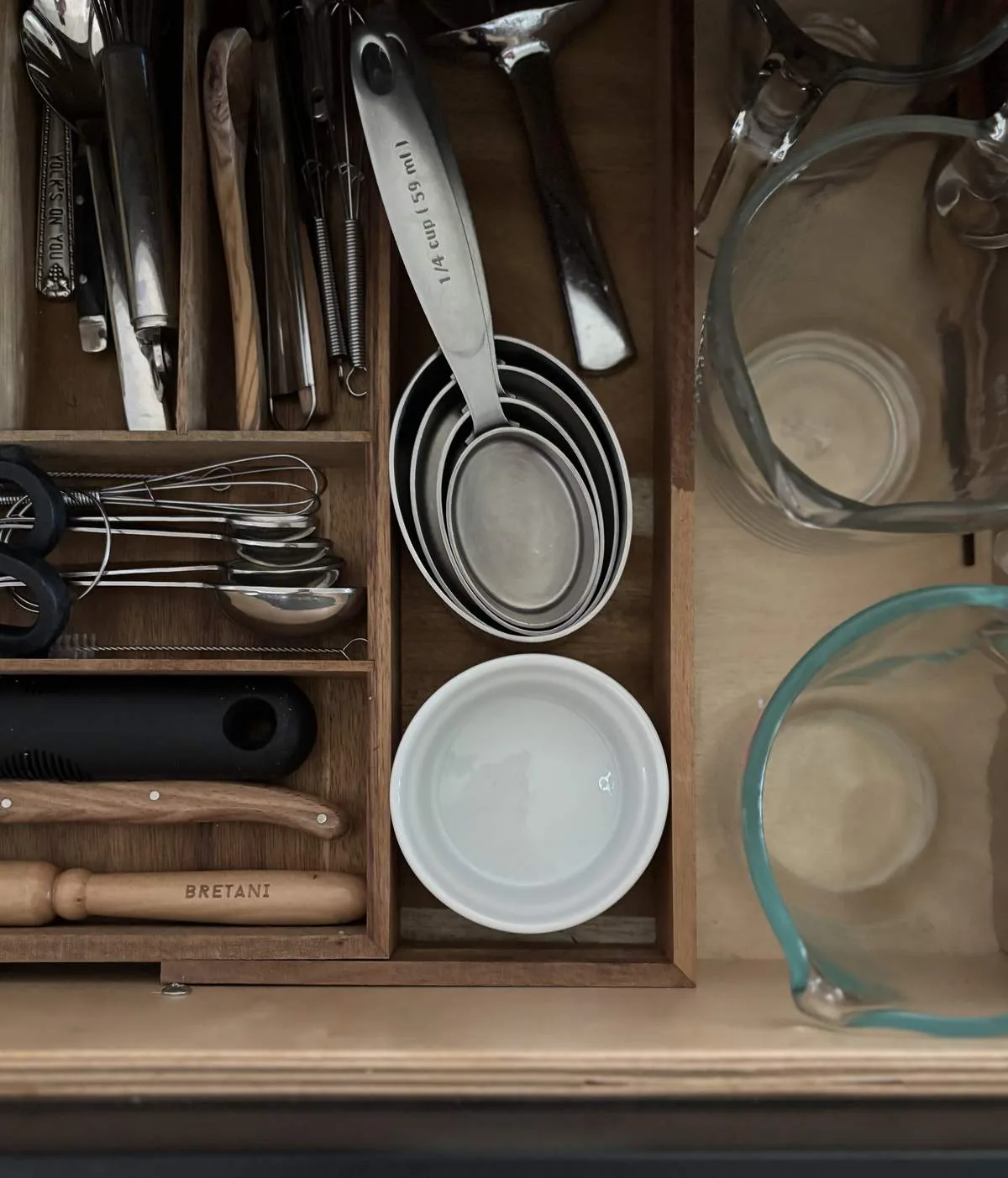 A neatly organized kitchen drawer containing measuring spoons, whisks, ladles, and glass measuring cups