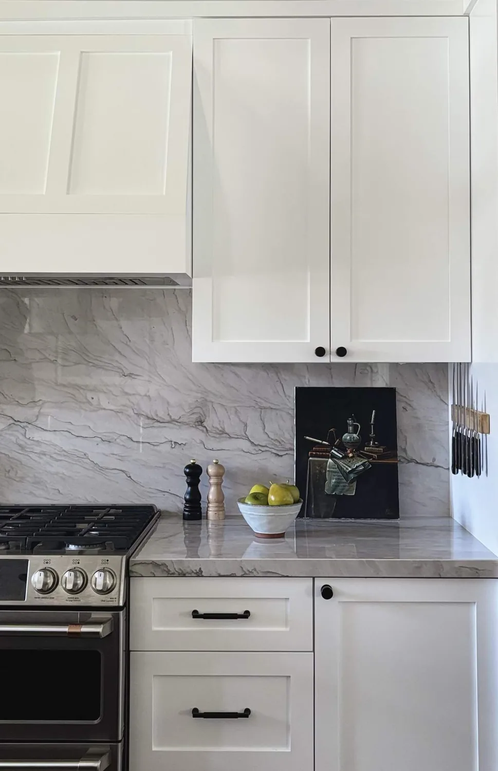 Think bright kitchen. White cabinets. Marble backsplash. Gas stove. Green apples on the counter