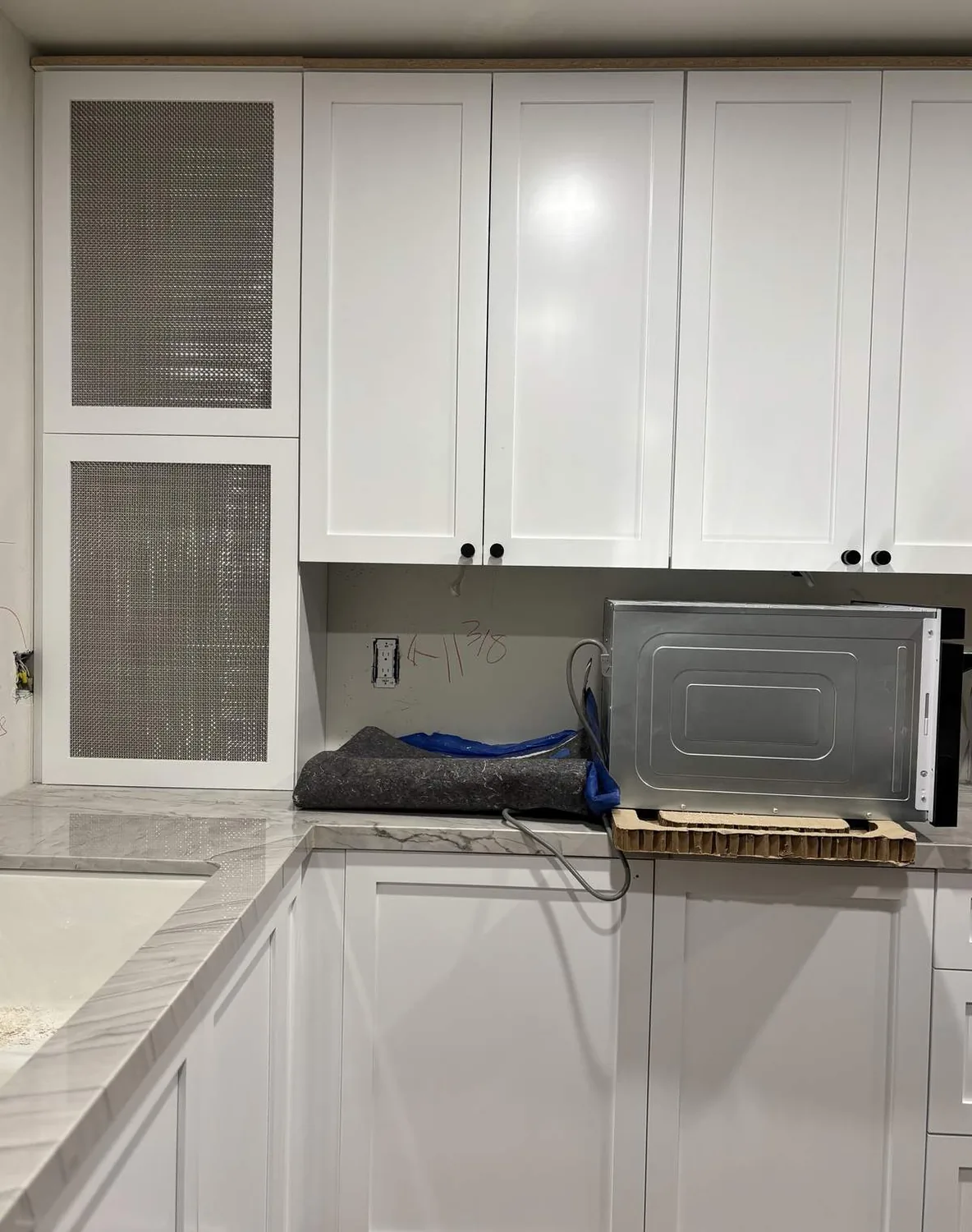 A kitchen corner with white cabinets, marble countertop, and a microwave placed on the counter during installation or