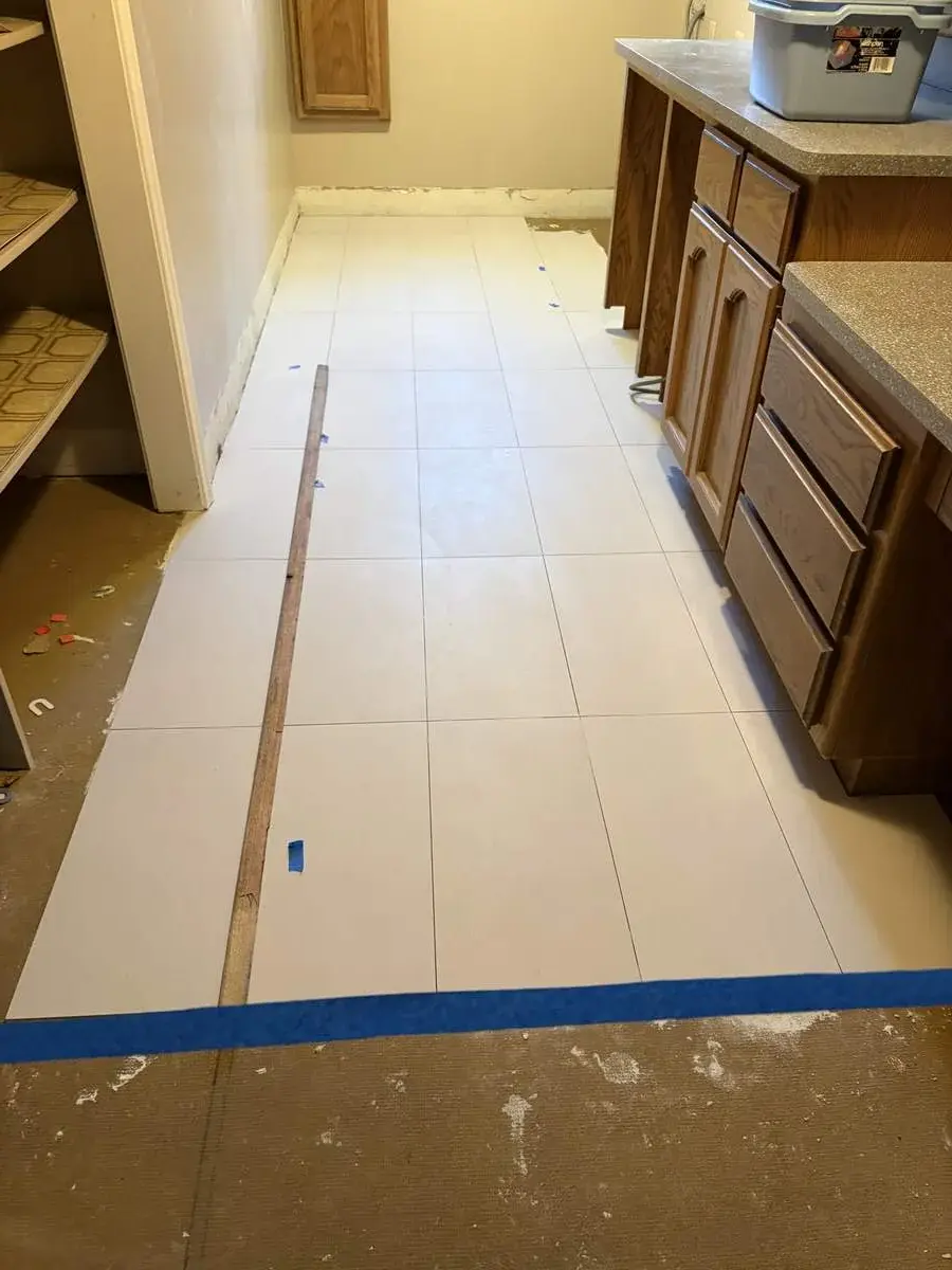 A kitchen under renovation with newly installed large white floor tiles and wooden cabinets