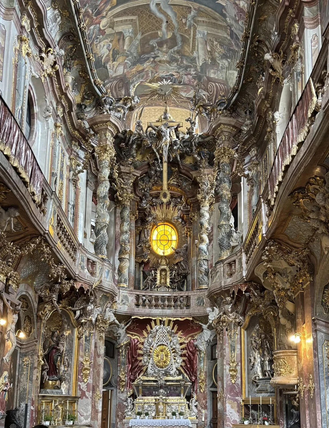 Baroque style? Sculptures, frescoes, all that gold. Feels like you could touch grandeur. The focal point is a large circular window casting light on an elaborately decorated altar