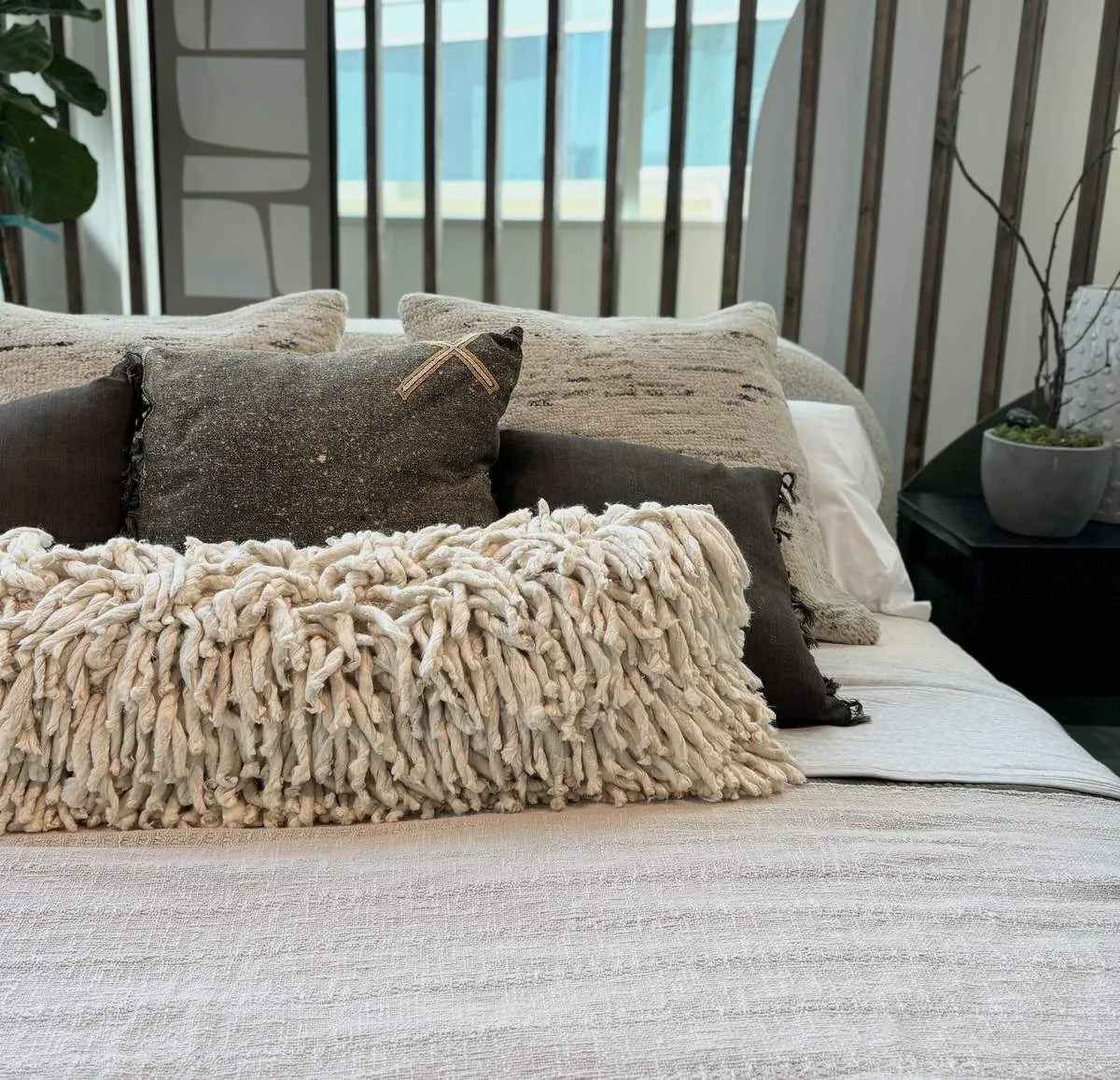 A close-up of a bed with multiple textured pillows and a neutral-colored blanket in a modern bedroom setting
