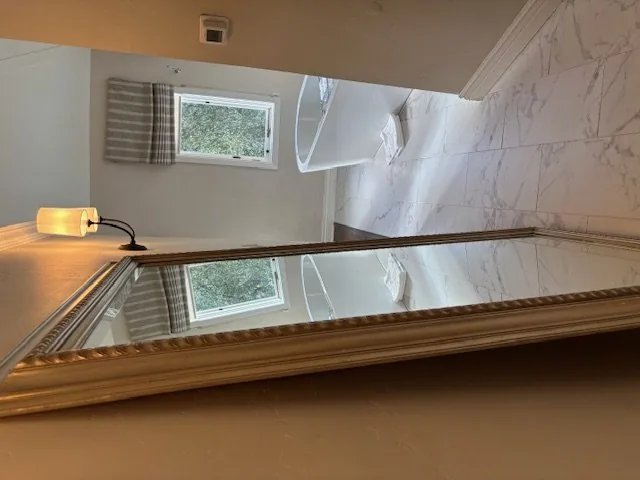 A modern bathroom with a freestanding bathtub, marble floor tiles, a large ornate mirror, and a wall-mounted light fixture